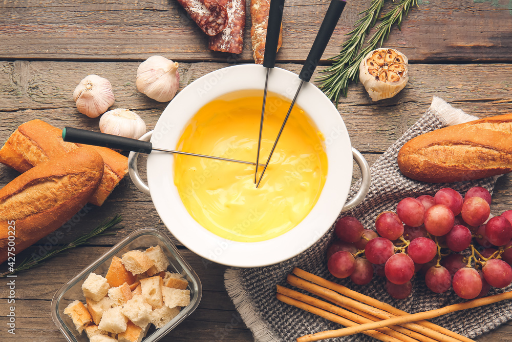 Cheese fondue and different snacks on wooden background