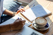 © VKVstudio - Young businessman writes notes in a project, he has a white mug with a hot latte, close up