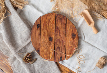 Round wooden cutting board made of rough boards on linen and burlap. Cones, a rope, a scoop for nuts lie nearby. 