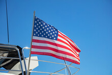 USA Flag On Pole On Ferry's Stern. Ongoing Cruise To Islands. Blue Sky Background