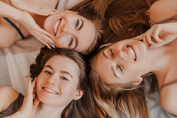 Women rest and have fun. Girlfriends laugh at home lying on the floor on pillows. Tree girls make homemade face and hair beauty masks. Women take care of youthful skin.