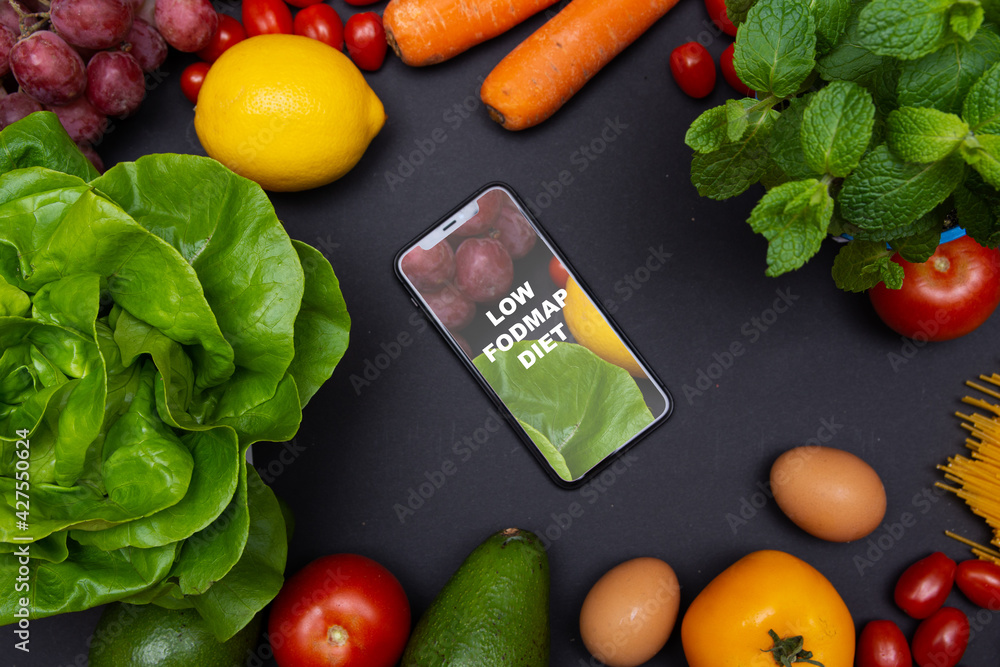Telefon z tekstem low FODMAP diet na ekranie, otoczony warzywami i owocami, zdrowa dieta i odżywianie - obrazy, fototapety, plakaty 