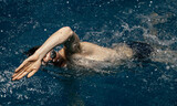 Fototapeta Łazienka - Caucasian athlete-swimmer crawls in the blue water. Portrait of a young male triathlete swimming in swimming goggles. Triathlon training concepts for triathletes