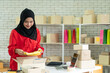 Young Entrepreneur Start-Up, A cheerful female Muslim seller packing an item into a parcel for shipping to a customer