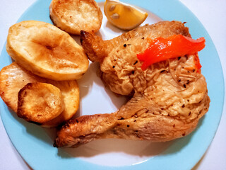 Sticker - Cooked chicken leg and roasted Spanish potatoes on a plate on a wooden background. Overhead shot