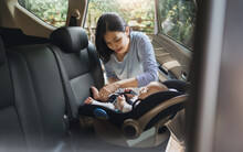 Asian Young Mother Putting Her Baby Son Into Car Seat And Fasten Seat Belts In The Car