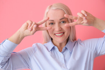 Wall Mural - Beautiful mature woman showing victory gesture on color background, closeup