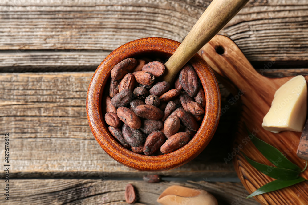 Bowl with cocoa beans on wooden background