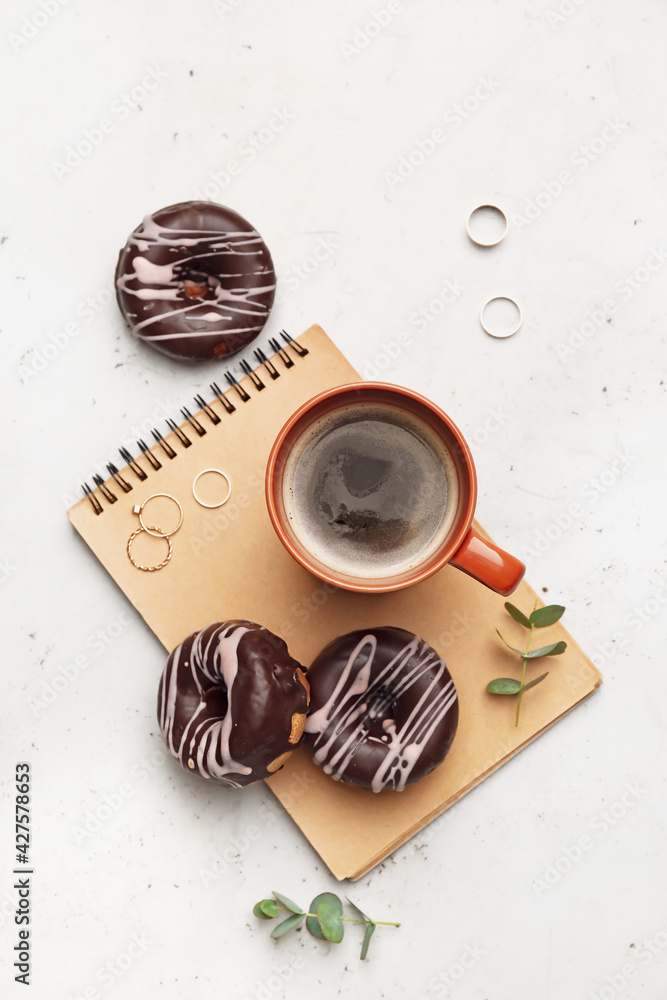 Notebook with cup of coffee and donuts on light background