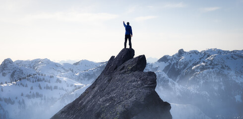 Composite. Adventurous Man Hiker on top of a Steep Rocky Cliff. over the Puffy Clouds. Sunset or Sunrise. Landscape Taken from British Columbia, Canada. Concept: Adventure, Explore, Hike, Lifestyle