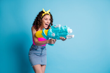 Sticker - Photo of crazy happy girl wear yellow headband jeans shoot water gun empty space isolated on blue color background