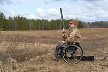 Hunter In A Wheelchair And Camouflage With Gun In His Hands Against The Background Of The Forest And Sky, April 2021
