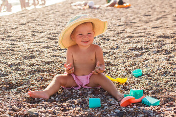 Smiling one-year-old girl sits on the sand