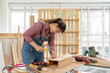 © godji10 - A Confident female carpenter uses a hammer and nail to hammering the wooden bar at the carpentry shop. Asian handywoman apprentice working in a workshop. DIY woodworking crafts and Hobby concepts.