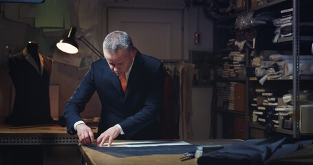 Cinematic shot of experienced tailor is measuring fine quality fabric for creation custom haute couture apparel in traditional tailoring atelier. Concept of handmade, couturier and tradition.	