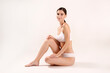 © Evrymmnt - Studio shot of fit woman wearing seamless underwear in seating on the floor isolated on white. Slim attractive female with flat belly in white lingerie. Copy space, close up, background.