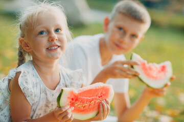 Wall Mural - Funny little toddler kids brother and sister eating watermelon on the park. Happy boy and girl together. Childhood, Family, Healthy Diet Concept.