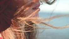 Close-up Of A Young Caucasian Woman's Hair Fluttering In Slow Motion In The Wind. Shallow Depth Of Field. Girl In Red Dress And Hat Dreamer Walk By The Sea