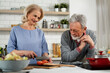 © JustLife - Senior woman and man cooking in the kitchen. Happy husband and wife preparing delicious food at home.