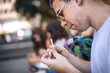© guruXOX - Addicted young man sitting on park bench and rolling cigarette, preparing to smoke