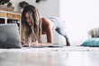 © simona - Young sporty woman working out at home, teenager doing fitness exercises on living room floor for buttocks body shaping using online personal training program with computer, doing workout pilates