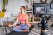 © simona - Young woman exercising at home doing pilates and recording at her with digital camera to teach workout and produce web class - content creator business free healthy lifestyle people concept