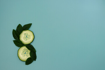 Wall Mural - Cucumber circles and green mint leaves are laid out in the shape of the number eight. Cucumbers on a blue background. 