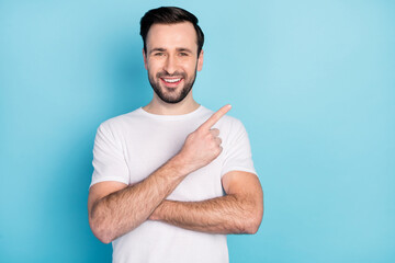 Photo of positive young man beaming smile indicate finger empty space isolated on blue color background