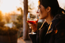 Young Woman With A Glass Of Red Wine In Sunset Light At A Terrace.