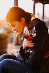 Wall Mural - Sad lonely woman with a glass of red wine in sunset light at a terrace.