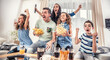 Family watching sports match on tv at home, cheering and shouting goal with hands up, spilling chips and popcorn from excitement