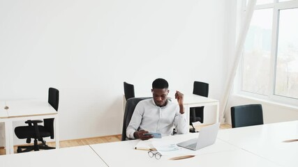 Sticker - A happy black guy with earbuds is using his smartphone while sitting in the office