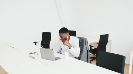 Wall Mural - A serious black guy with earbuds is working with paper documents and laptop computer sitting in the office