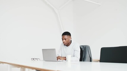 Poster - An attractive black guy with earbuds is working with paper documents and laptop computer sitting alone in the office