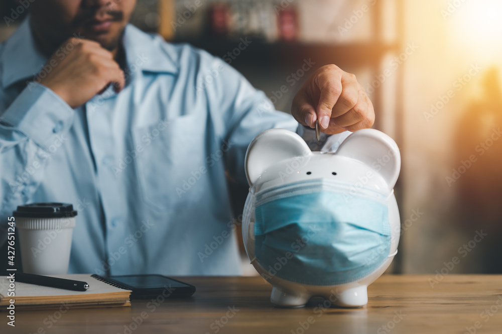 businessman putting coin on piggy bank wearing surgical face mask. Global economy during coronavirus pandemic. Financial crisis, Financial Despair, banking concept. saving and investment. - obrazy, fototapety, plakaty 