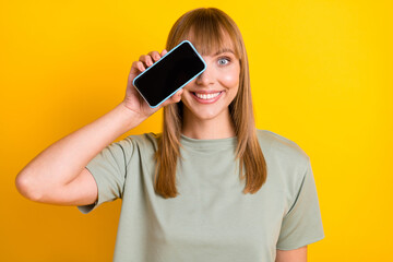 Wall Mural - Close-up portrait of lovely cheerful girl demonstrating gadget having fun closing eye isolated over bright yellow color background