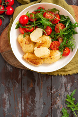 Wall Mural - Baked potatoes and salad in a plate on a dark wooden background top view. Tasty rustic lunch or dinner, vegan food. Baked potatoes with tomatoes, arugula, and spices. Copy space for text