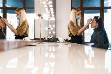 Blonde woman in face mask doing makeup for her client in beauty salon