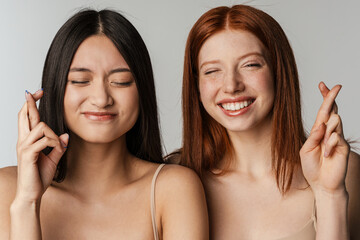 Wall Mural - Multiracial two women smiling and holding fingers crossed for good luck