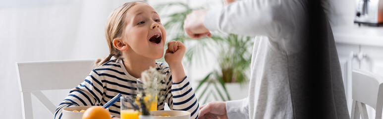 Wall Mural - father feeding daughter during breakfast in kitchen, blurred foreground, banner