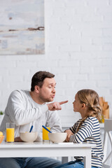 Wall Mural - father pointing at nose of daughter while having fun during breakfast