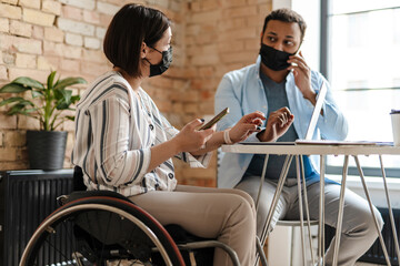 Multiracial two colleagues in face mask using smartphone while working