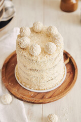 Poster - Closeup shot of a yummy white cake with coconut flakes and balls covering it on a wooden tray