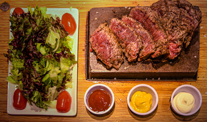 Wall Mural - freshly cut piece of steak on the hot stone with sauces and side salad