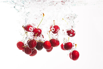 Wall Mural - Red cherries splashing into crystal clear water with air bubbles. Isolated on a white background.