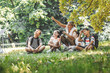 Group of school kids sitting on grass in forest with they teacher.They learning about nature and wildlife.	
