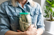 © Angelov - Happy woman in gray jersey holding bank with dollar cash, looking at camera, isolated over beige background