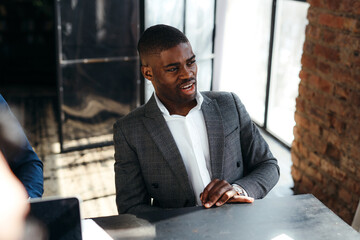 Wall Mural - African American manager smiling broadly while sitting at the table at the meeting and talking with colleagues