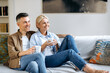 © Kateryna - Loving happy adult married caucasian couple in stylish casual clothes, happy husband and wife sitting on the comfortable sofa in the living room, holding cups of tea, chatting, spending time at home