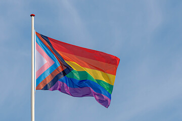 Worldwide LGBTQ community concept with progress pride flag (new design of rainbow flag) waving in the air with blue sky, Celebration of gay pride, The symbol of lesbian, gay, bisexual and transgender.